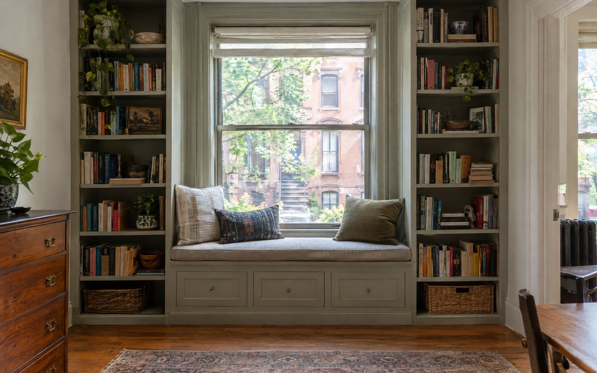 Painted built-in bookcases framing a cushioned window seat in a Brooklyn brownstone, design concept