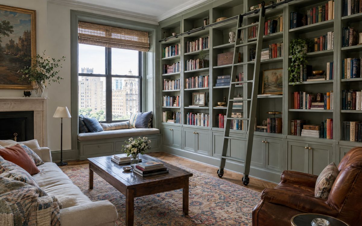 Wall-to-wall painted bookcases with a rolling ladder and window seat in an Upper West Side apartment, design concept